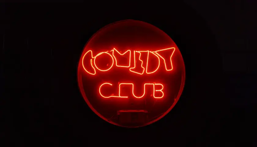 Rotes Neonschild "COMEDY CLUB" im Dunkeln. Ein Ort, an dem die Bedeutung von Kabarett durch Lachen und Unterhaltung lebendig wird.
