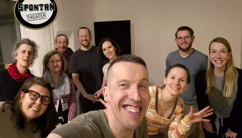 Gruppe lacht in die Kamera, bereit, die **improvisieren Bedeutung** im Spontan Theater zu leben.