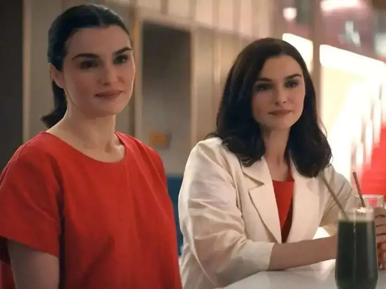 Zwei Frauen, die sich ähneln, stehen nebeneinander. Die eine trägt ein rotes Oberteil, die andere einen beigen Blazer über einem roten Kleid. Sie sind Teil von "die unzertrennlichen serie".