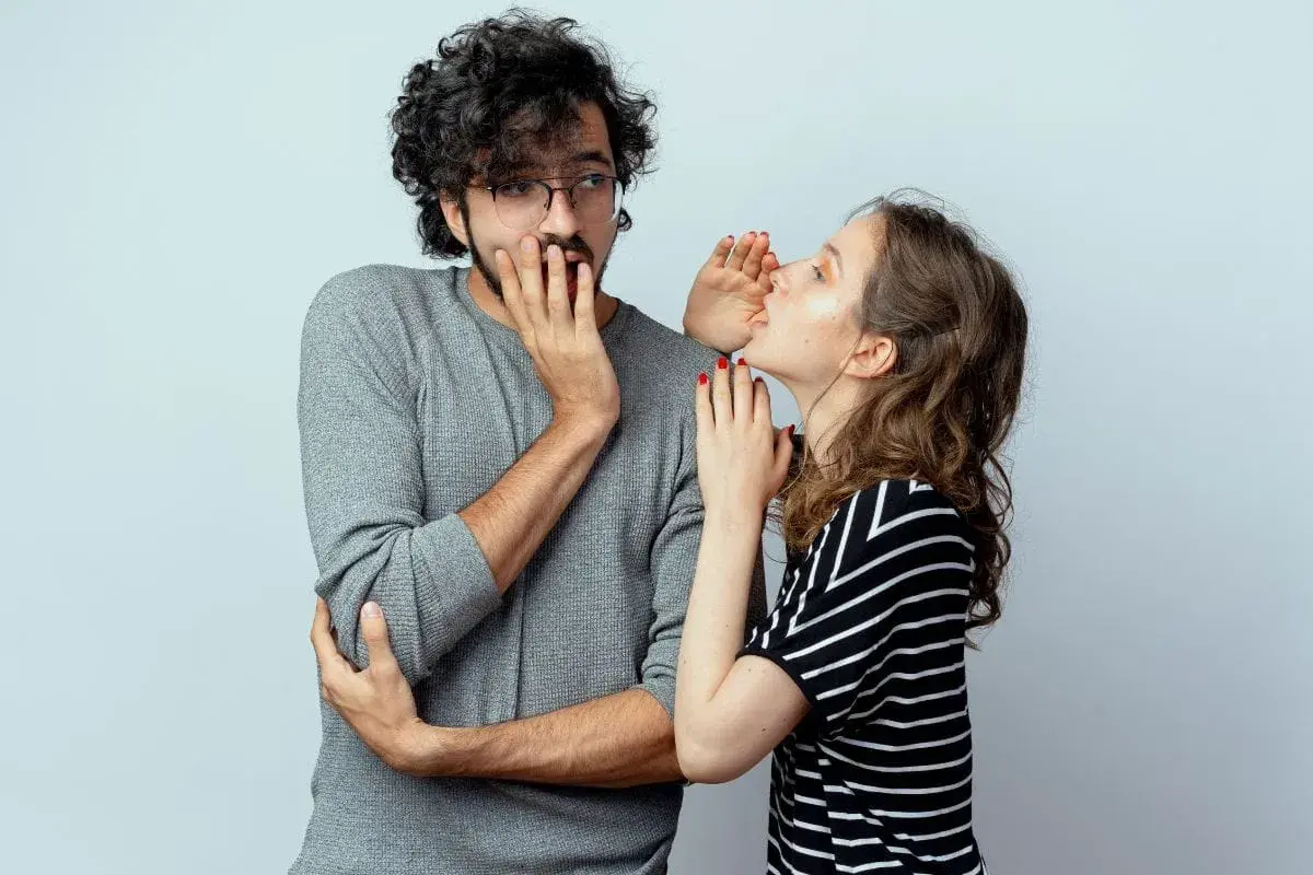 Sie flüstert ihm etwas ins Ohr, sein Gesichtsausdruck deutet auf ein **double entendre** hin.