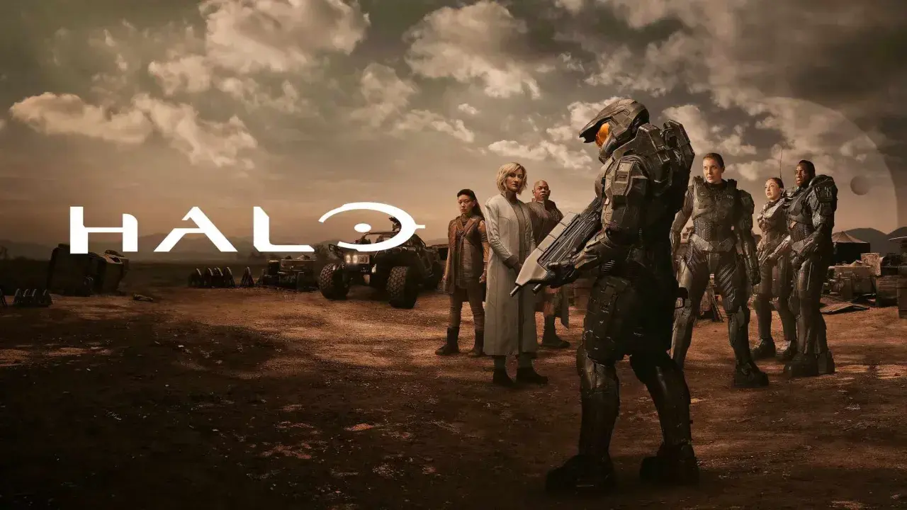 Die Besetzung von Halo (Fernsehserie) steht in einer staubigen Landschaft. Im Vordergrund ein Master Chief, im Hintergrund das Halo-Logo und weitere Charaktere.