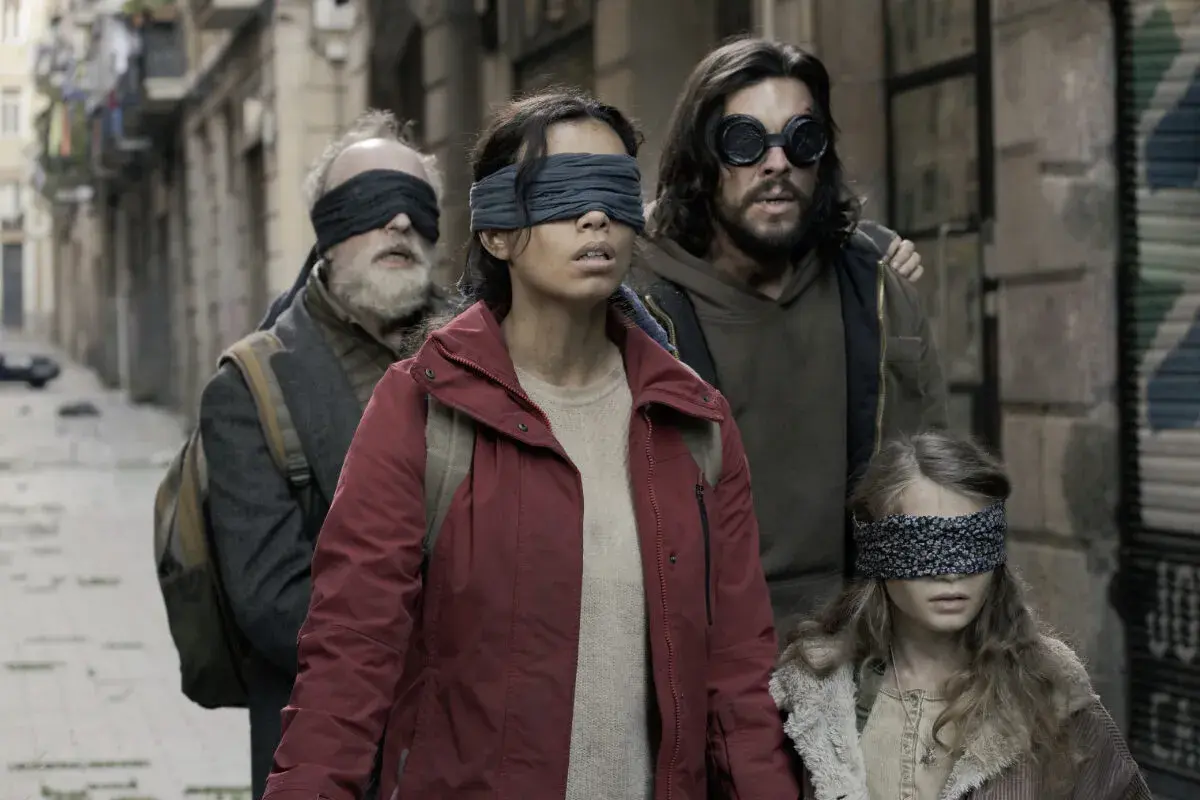 Die Besetzung von Bird Box: Eine Gruppe von Menschen, die mit verbundenen Augen durch eine Gasse gehen, um den unsichtbaren Gefahren zu entkommen.