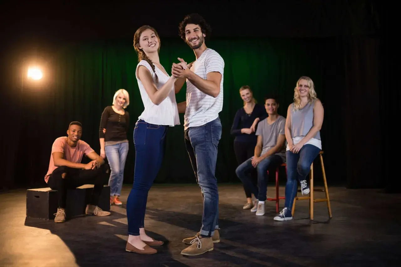 Ein Paar tanzt im Scheinwerferlicht, während andere Teilnehmer eines Improvisationstheater Kurses im Hintergrund sitzen und zuschauen.