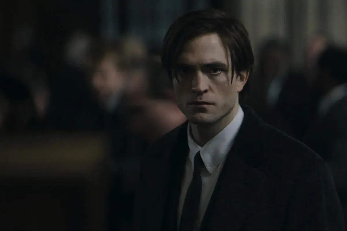 Robert Pattinson als der junge Batman, mit ernstem Blick und dunklem Anzug, inmitten einer Menge.