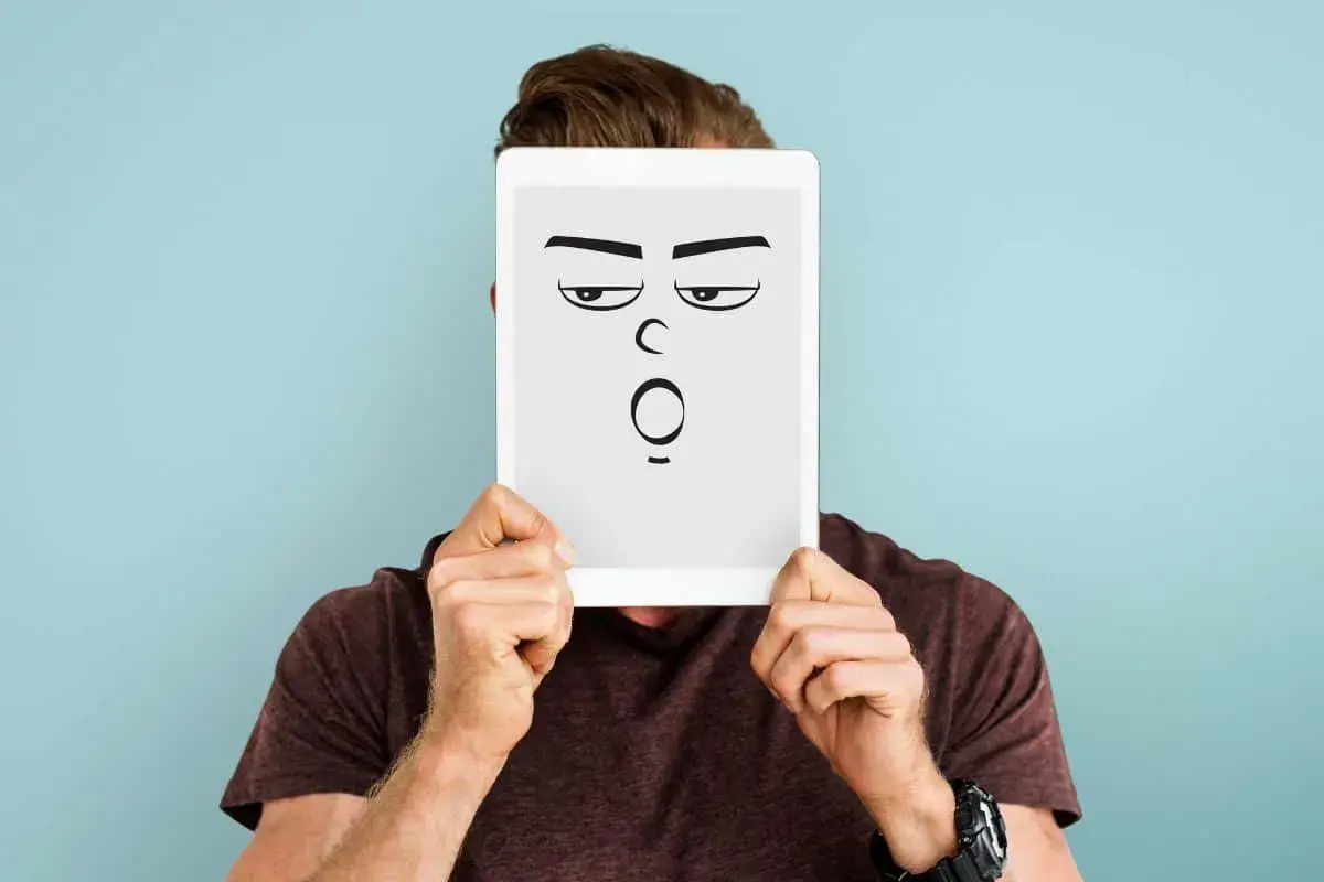 Mann hält Tablet mit cartoonhaftem Gesicht, das genervt und überrascht schaut. Perfekt für die sarkasmus definition.