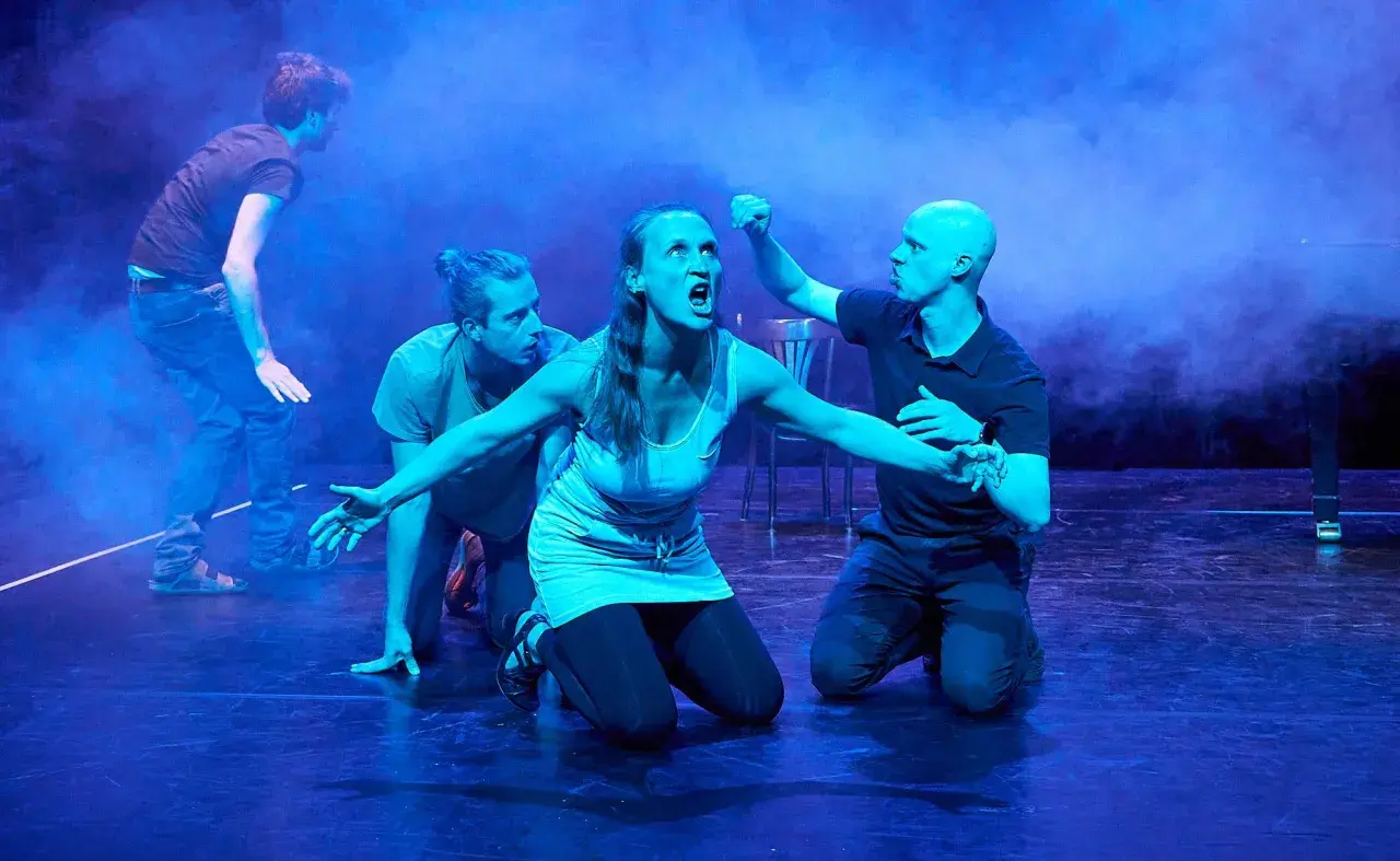 Dramatische Szene mit vier Darstellern auf einer Bühne. Eine Frau schreit, umgeben von drei Männern. Typische Merkmale eines Musicals: Emotion, Bewegung und Inszenierung.