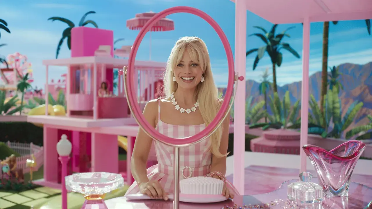 Margot Robbie als Barbie im Film, lächelnd durch einen pinken Spiegel, umgeben von einer rosafarbenen Traumwelt.