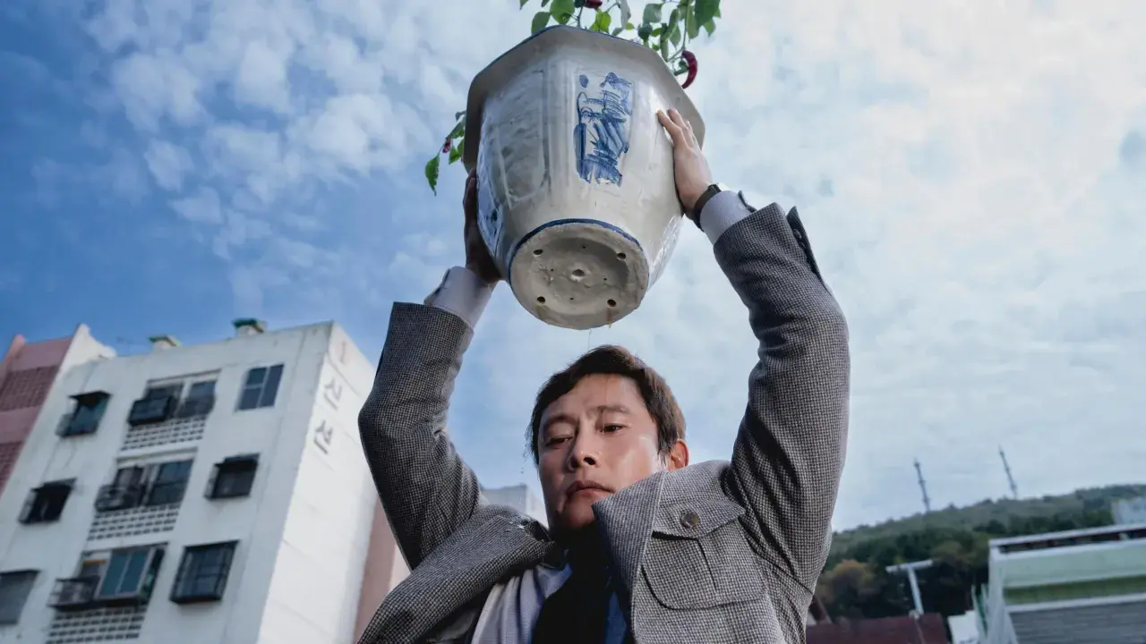 Ein Mann hält einen Blumentopf über seinem Kopf. Wasser tropft herunter. Eine Szene aus dem Film "No other choice".