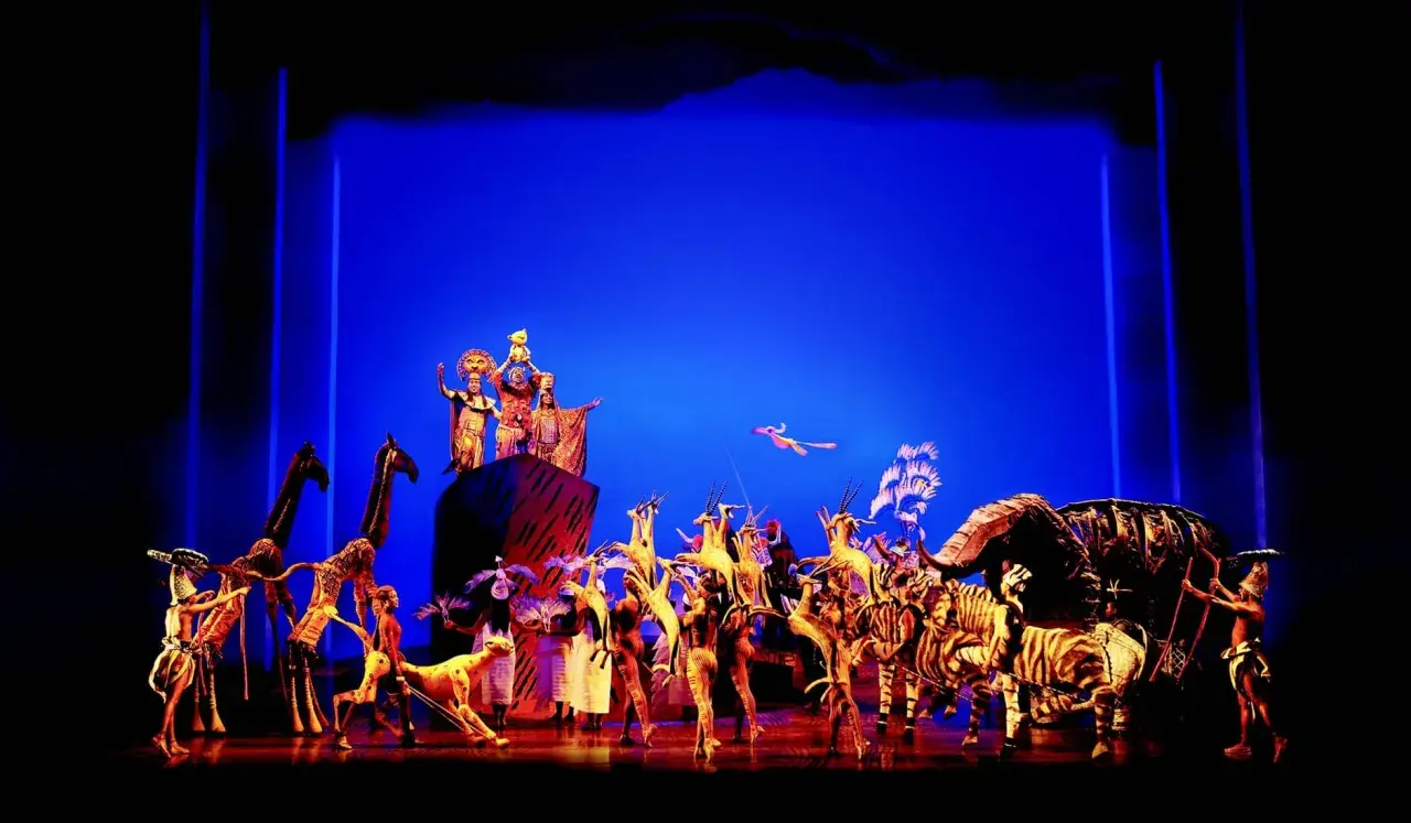 Bühnenszene mit Darstellern in Tierkostümen und Figuren, die den Beginn eines Musicals in Deutschland feiern.