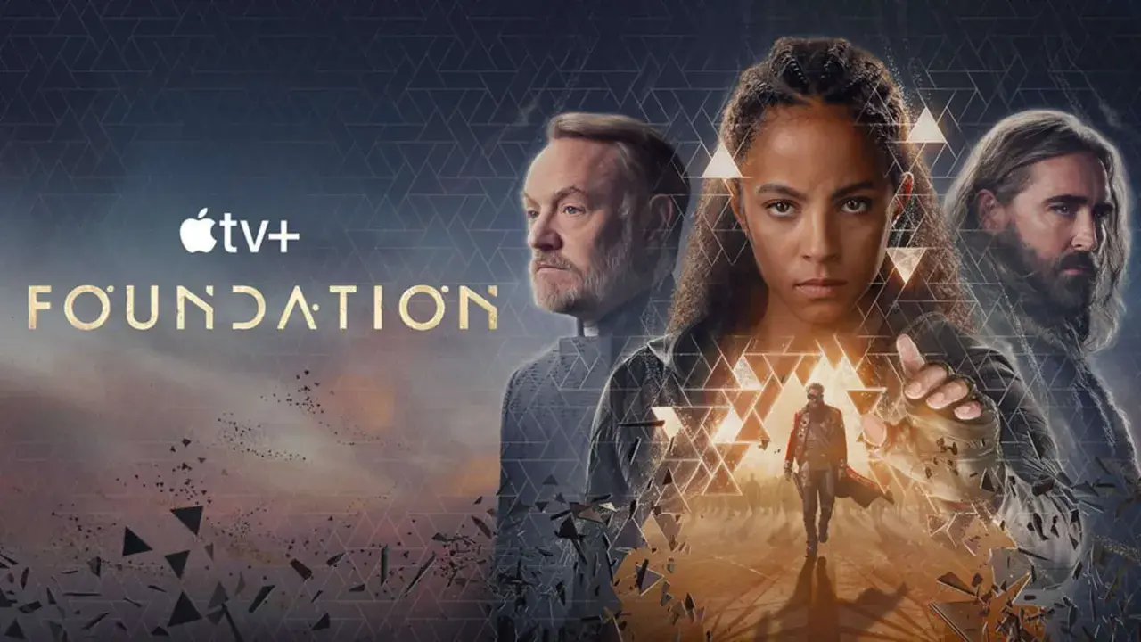 Apple TV+ "Foundation" Serie: Drei Hauptfiguren blicken ernst in die Ferne, während ein Mann im Vordergrund eine Hand ausstreckt.