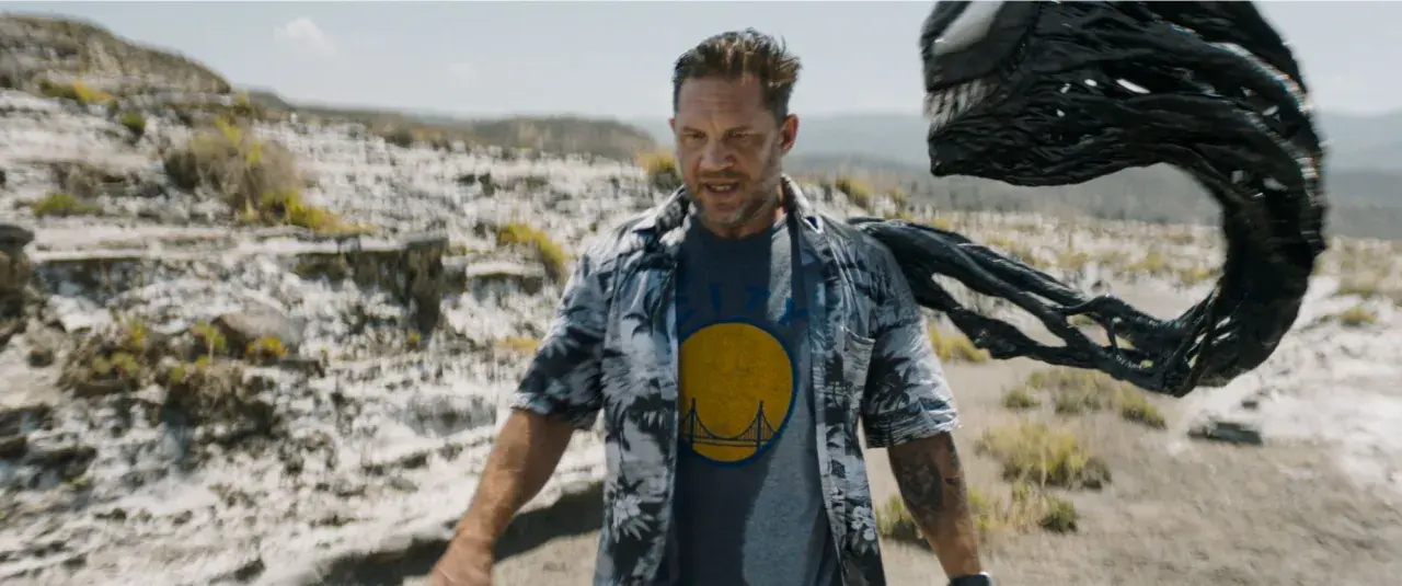 Tom Hardy als Eddie Brock, mit Venom, der sich hinter ihm im Ödland windet. Ein Blick auf die Besetzung von Venom: The Last Dance.