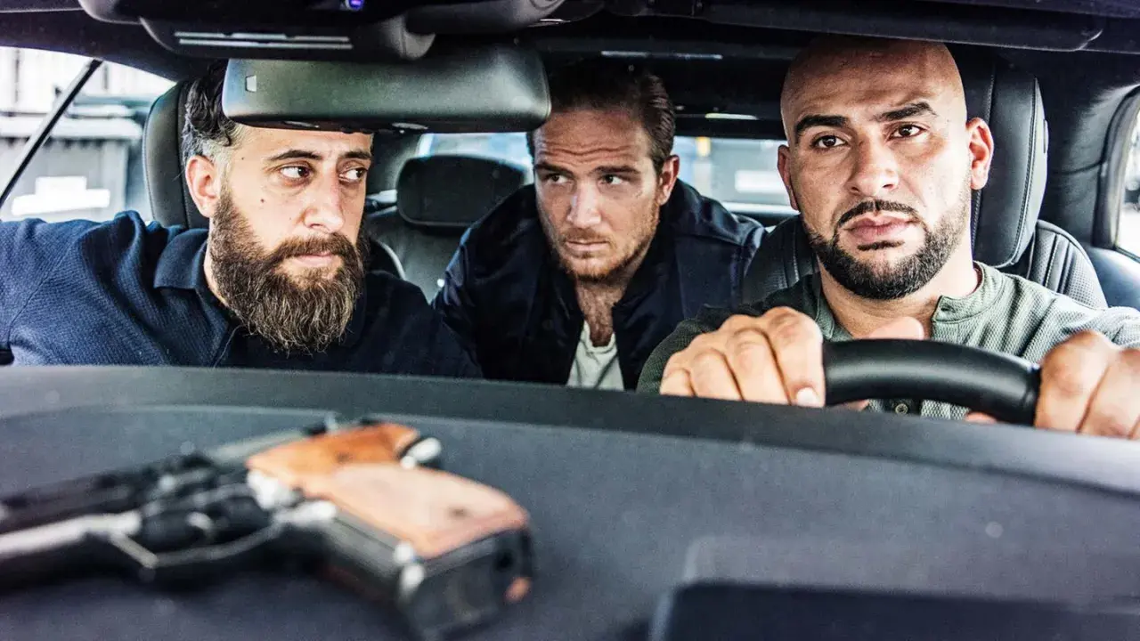 Drei Männer, die wie 4 Blocks Schauspieler aussehen, sitzen in einem Auto. Eine Pistole liegt auf dem Armaturenbrett.