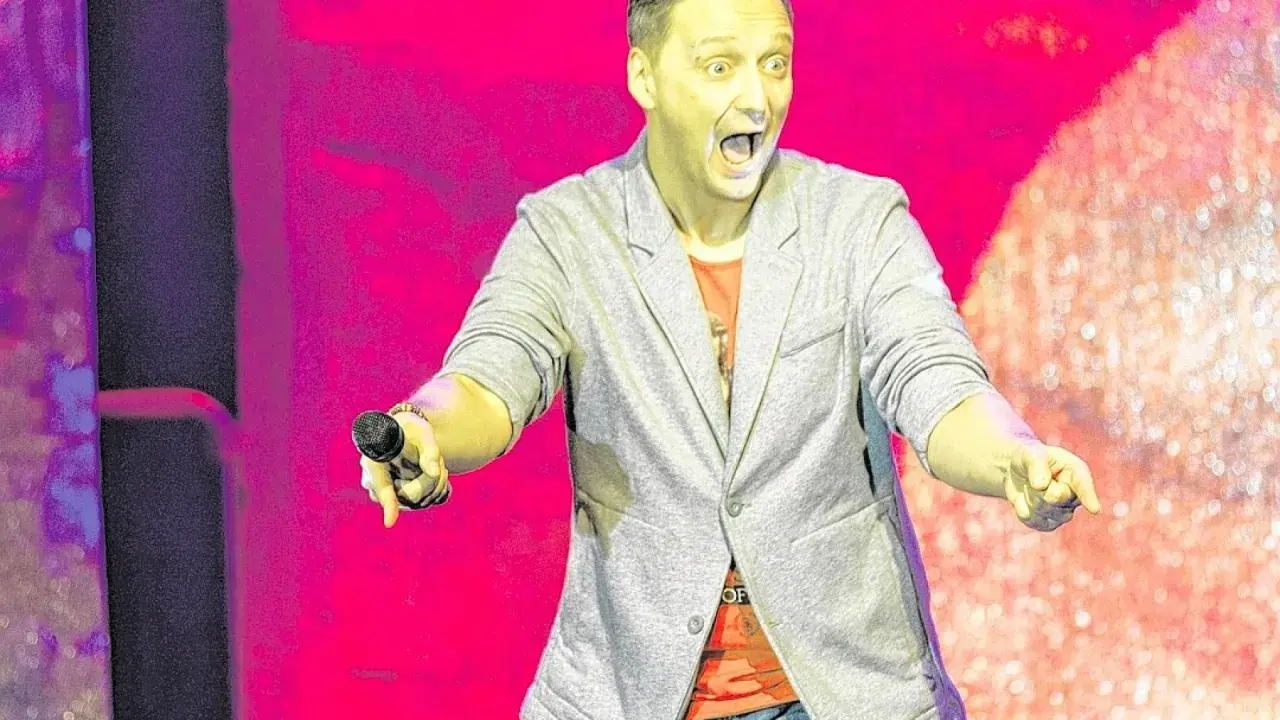 Ein Mann mit offenem Mund und Mikrofon in der Hand, der eine lebhafte Performance liefert – das ist die Essenz von Kabarett.