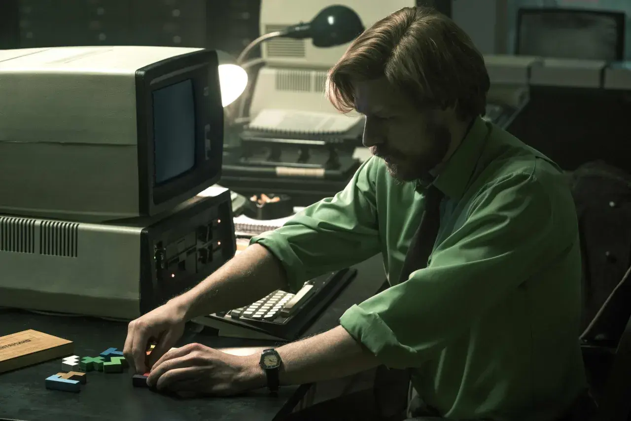 Mann mit Bart spielt mit Tetris-Steinen vor einem alten Computer. Ein Moment aus dem "Tetris"-Film.
