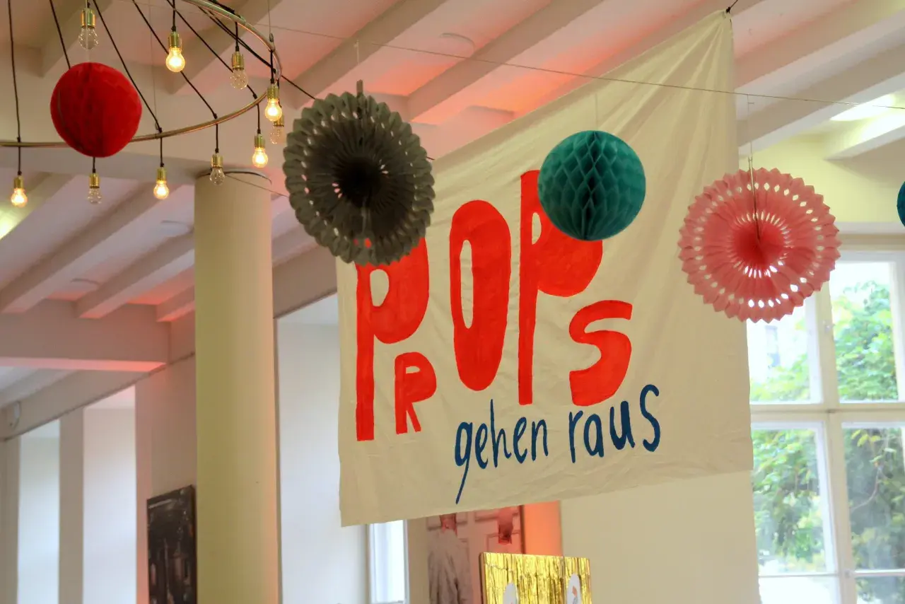 Bunte Papier-Props und eine Fahne mit der Aufschrift "POPS gehen raus" hängen von der Decke.
