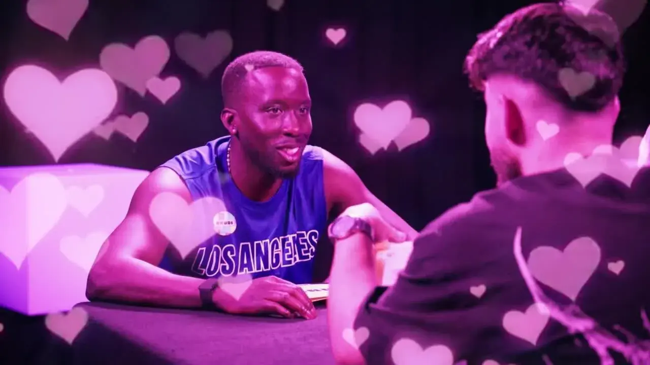 Zwei Männer im Gespräch, umgeben von rosa Herzen. Einer trägt ein blaues Tanktop mit "Los Angeles". Der Vibe ist wie ein "roasted jugendsprache" Date.