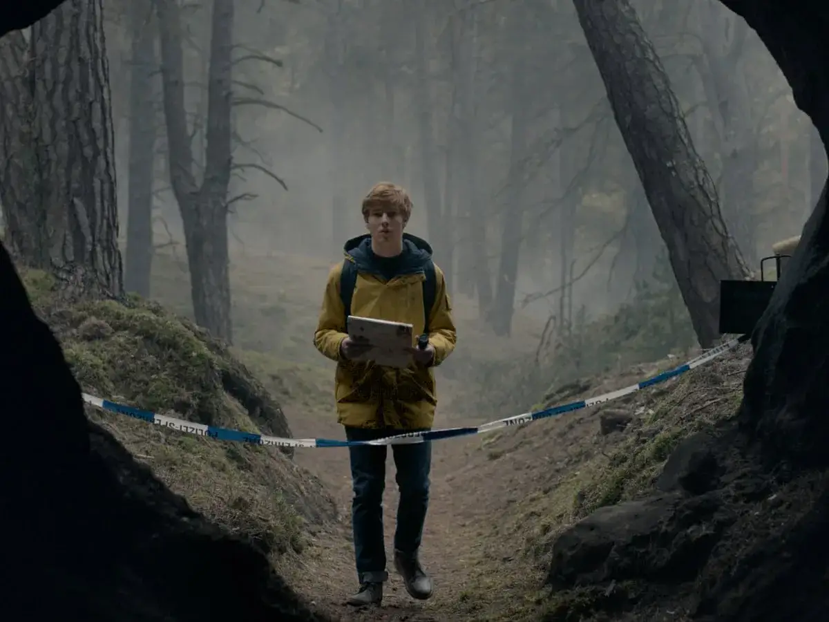 Jonas, mit seinem gelben Mantel, durchquert einen nebligen Wald, vorbei an Absperrband. Sein Weg ist unberechenbar, die Suche nach Antworten beginnt.