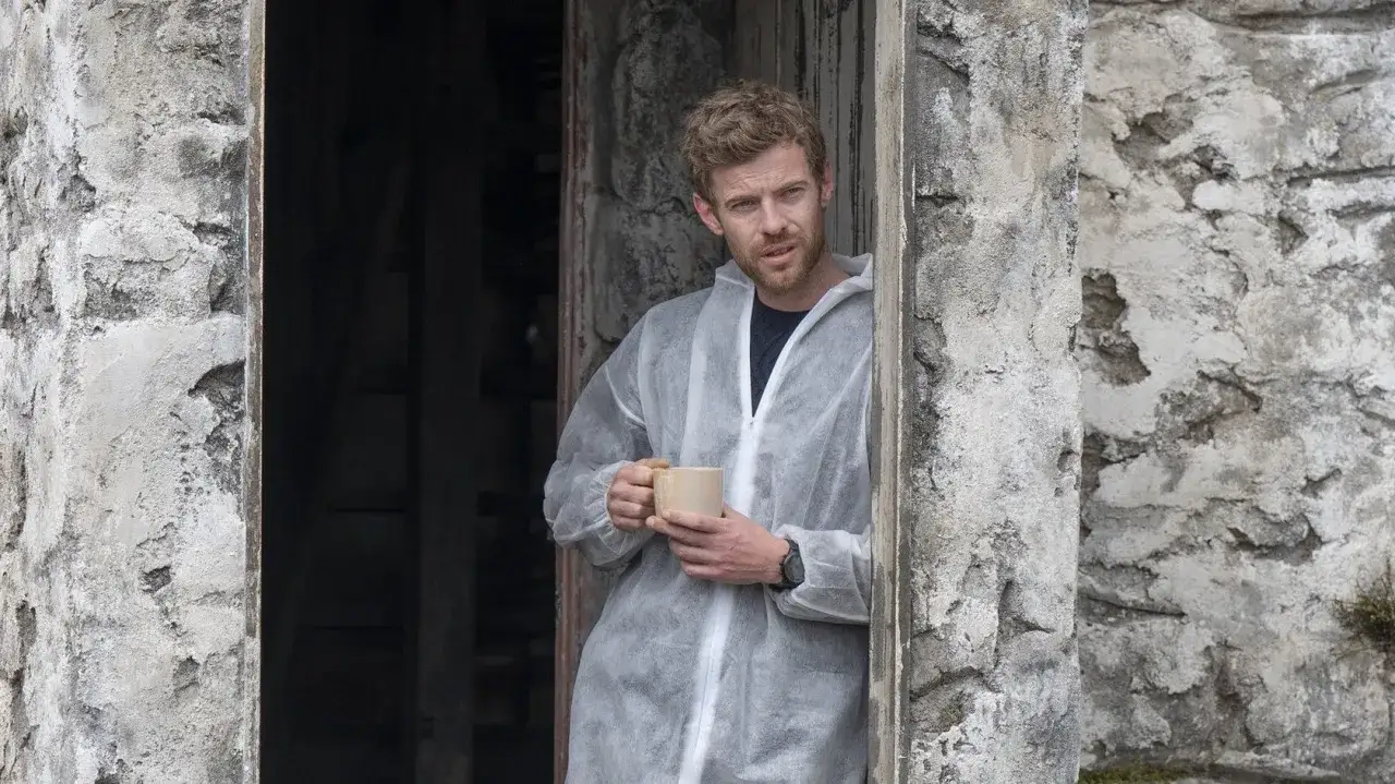 Mann in Schutzanzug hält Tasse, ein Moment der Ruhe in der Serie