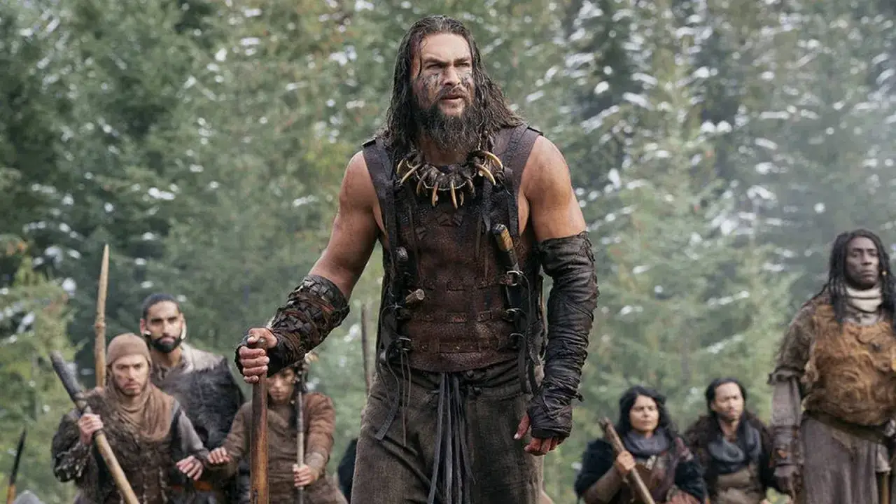 Jason Momoa als Krieger mit Kriegsbemalung und einem Halsband aus Knochen, umgeben von seiner Gruppe. Ein starker Moment aus der serie.