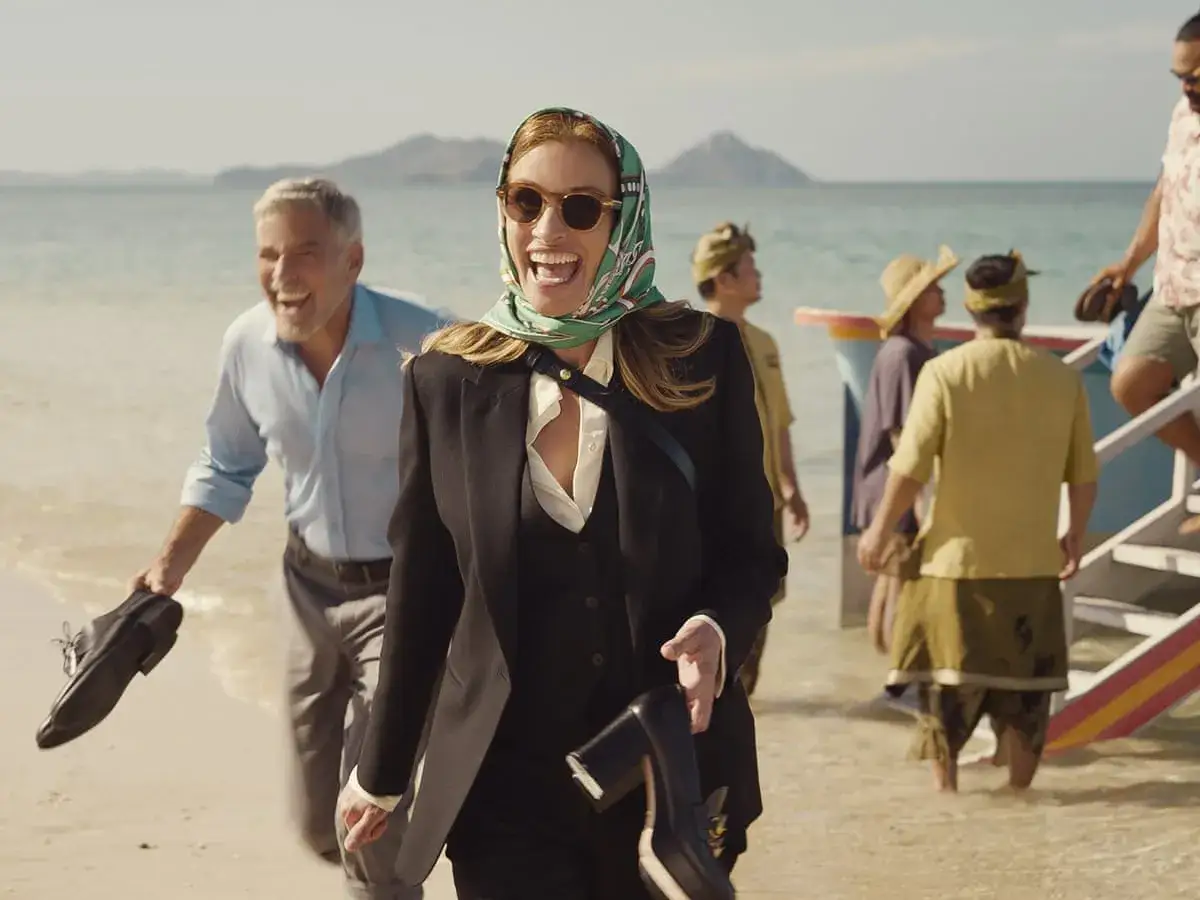 Julia Roberts und George Clooney genießen ihren Ticket ins Paradies am Strand. Sie laufen lachend im Wasser, während im Hintergrund weitere Personen zu sehen sind.