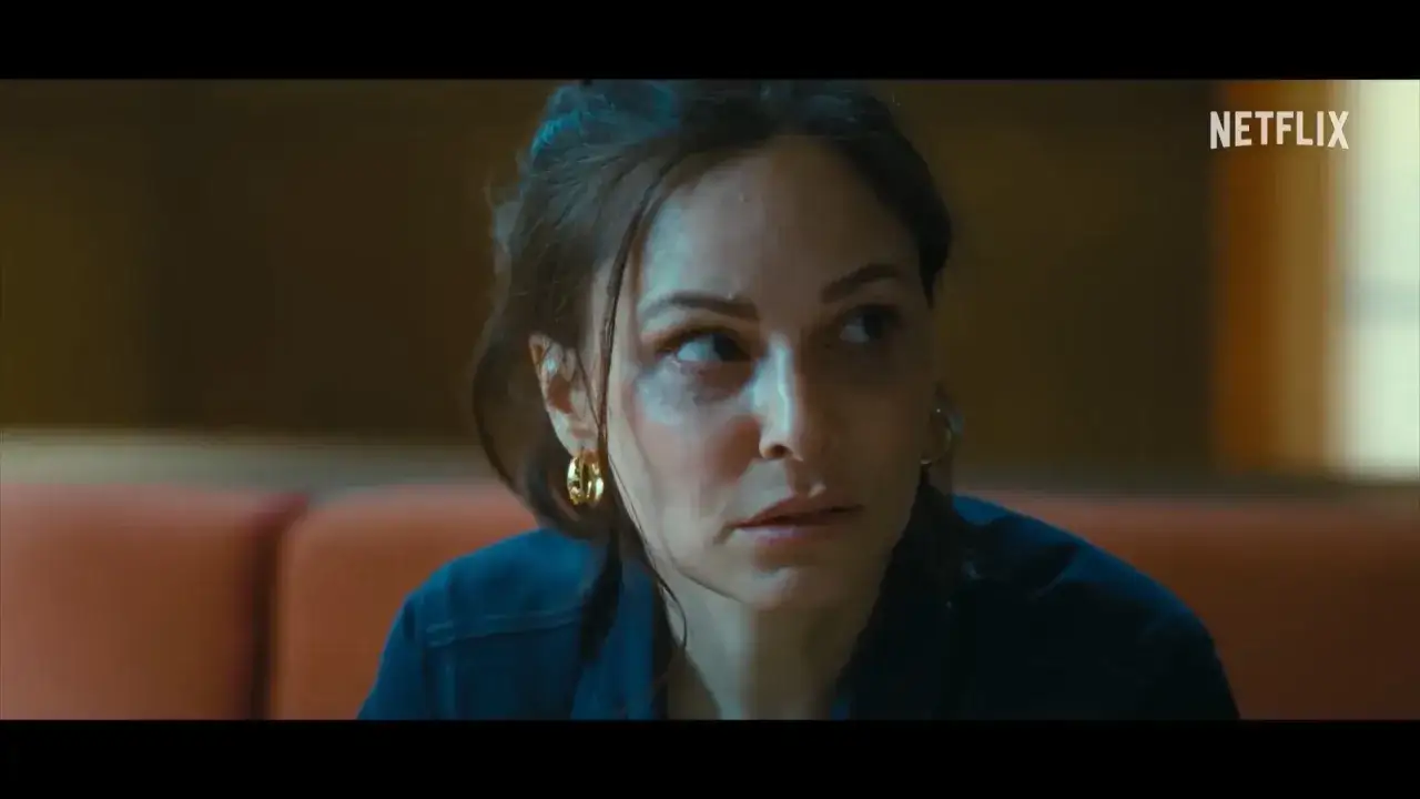 Eine Frau mit dunklen Augenringen und goldenen Ohrringen blickt besorgt. Die besetzung von Cassandra scheint eine dramatische Rolle zu spielen.