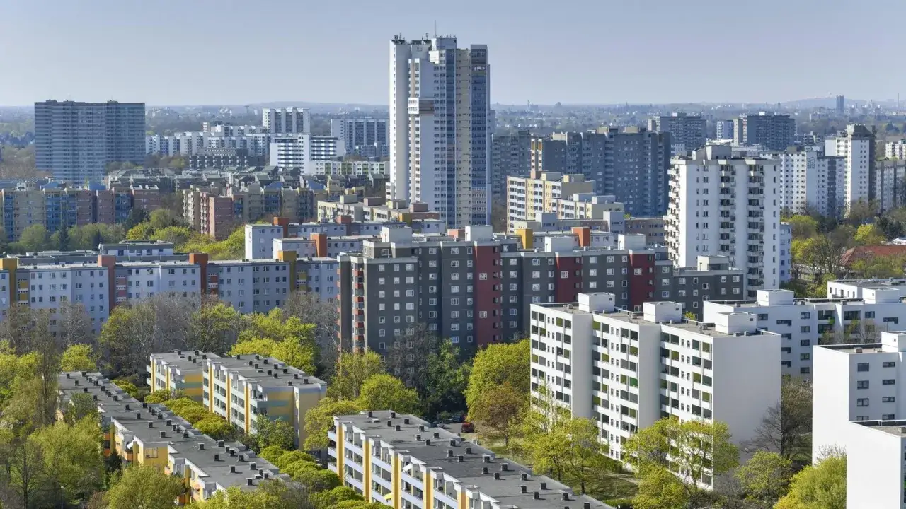 Sonne und Beton: Ein Meer aus Wohnblöcken, durchbrochen von grünen Bäumen. Die Sonne wirft lange Schatten auf die grauen Fassaden.