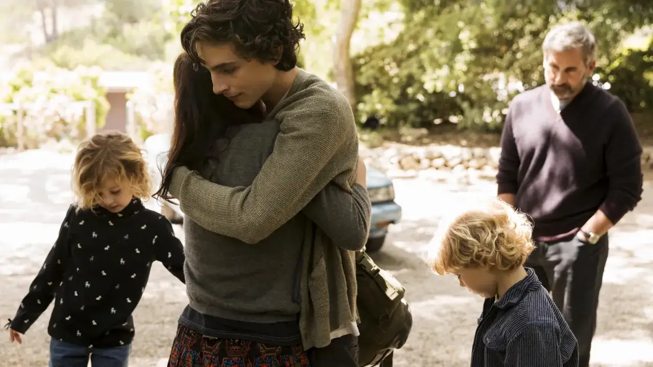 Ein schöner Junge umarmt jemanden, während zwei Kinder und ein Mann im Hintergrund stehen. Ein Moment aus einem bewegenden Film.