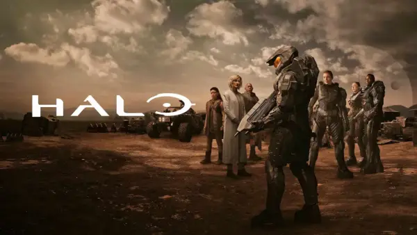 Die Besetzung von Halo (Fernsehserie) steht in einer staubigen Landschaft. Im Vordergrund ein Master Chief, im Hintergrund das Halo-Logo und weitere Charaktere.