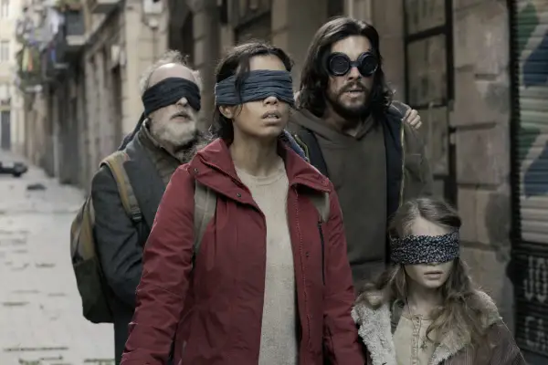 Die Besetzung von Bird Box: Eine Gruppe von Menschen, die mit verbundenen Augen durch eine Gasse gehen, um den unsichtbaren Gefahren zu entkommen.