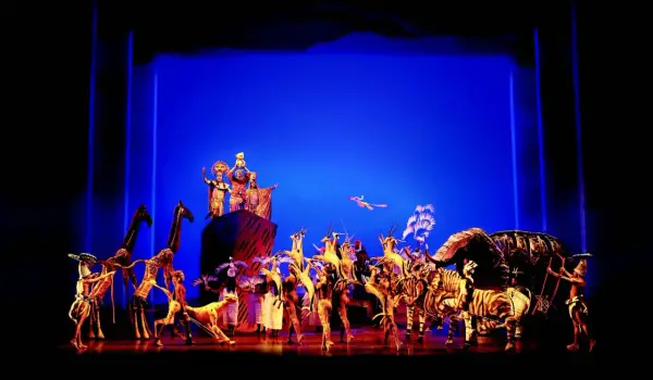 Bühnenszene mit Darstellern in Tierkostümen und Figuren, die den Beginn eines Musicals in Deutschland feiern.